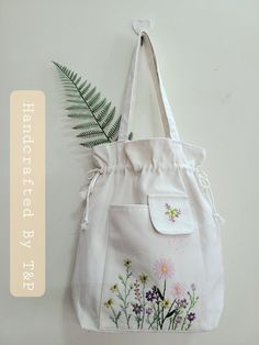 a white tote bag with flowers on it and a fern in the corner next to it