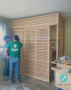 two men standing in front of a wall made out of wooden slatted boards