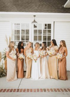 a group of women standing next to each other in front of a white house holding bouquets