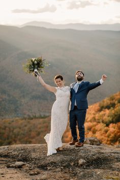 a bride and groom standing on top of a mountain with their arms in the air