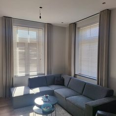 a living room filled with furniture next to two large windows covered in shades of light