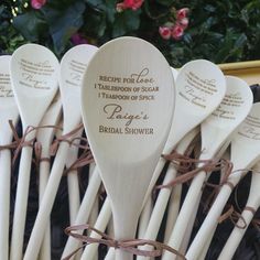 white wooden spoons with brown writing on them are lined up in a basket next to pink flowers