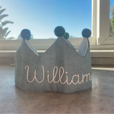 a small gray crown with the word william on it sitting on a table in front of a window