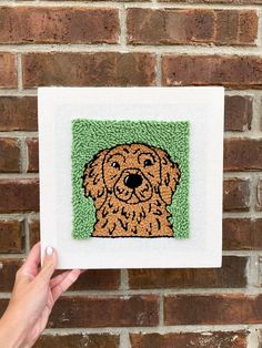 a hand is holding up a small cross stitch picture with a dog's face on it