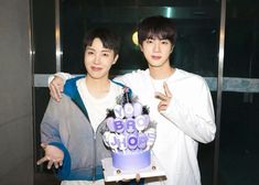 two young men standing next to each other while holding a cake in front of them