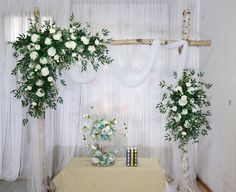 a table topped with flowers and greenery next to a white drape covered wall