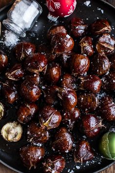 a plate filled with cooked chestnuts next to an apple and pepper shaker on a wooden table