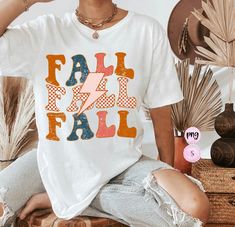 a woman sitting on the floor wearing a white shirt that says fall