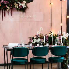 a long table with green chairs and flowers on the wall behind it is surrounded by candles