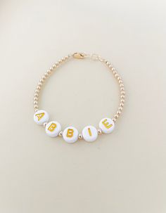 This beautiful personalized gold filled name bracelet is a perfect gift for anyone! Mamas, toddlers and children love these custom bracelets made to last. Our Bracelets are Handmade in the USA and are made with high quality gold & white letter beads with gorgeous pearl beads and 14K gold filled attachments. You will enter the custom name in the text box before adding to the cart. They are beautiful and add the perfect amount of dress up to every outfit. Each bracelet has extra links for room to Personalized Name Bracelets, Personalized Name Bracelet With Round Beads For Birthday, Personalized Round Beads Name Bracelet For Birthday, Gold Beaded Bracelet With Name For Birthday, Adjustable Yellow Gold Name Jewelry, Personalized Hypoallergenic Yellow Gold Bracelets, Gold Beaded Bracelets With Name For Birthday, Cute Custom Name Bracelet Jewelry, Gold Round Name Bracelet