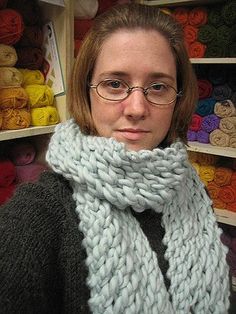 a woman wearing glasses and a knitted scarf in front of shelves with yarns