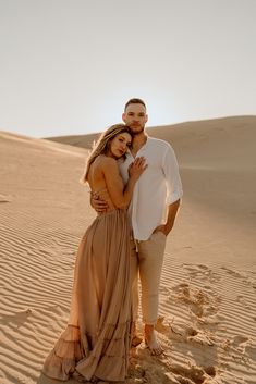 a man and woman are standing in the sand at sunset, posing for a photo