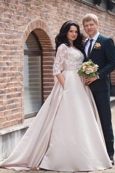 two people standing next to each other in front of a brick wall wearing wedding dresses