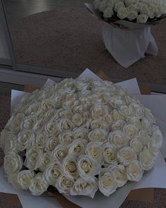 a large bouquet of white roses sitting on top of a table next to a mirror