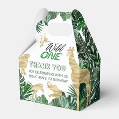 a white and green birthday box with giraffes on the front, palm leaves in the background