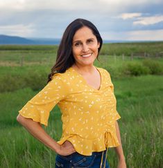 a woman standing in a field with her hands on her hips and smiling at the camera