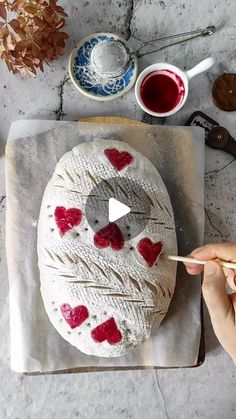 someone is decorating a cake with white icing and red heart shapes on it