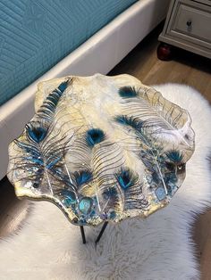 a glass table with peacock feathers on it sitting on a white rug in front of a bed