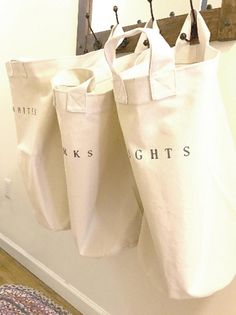 three white bags hanging from hooks on a wall next to a rug and door way mirror