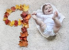 a baby is laying on the floor next to a cross made out of autumn leaves