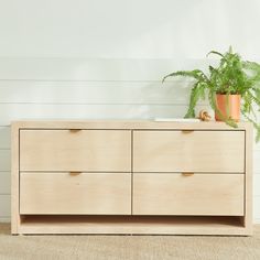 a wooden dresser with two potted plants on top and white walls in the background