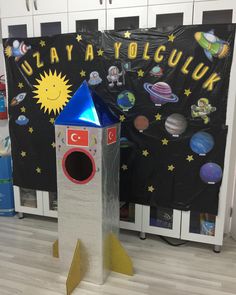 a cardboard rocket is sitting on the floor in front of a bulletin board with space and stars