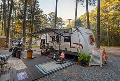 an rv is parked in the woods with its awning open and chairs around it