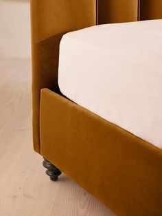 a close up of a bed with white sheets and brown headboard, on a wooden floor