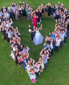 a large group of people standing in the shape of a heart on top of grass