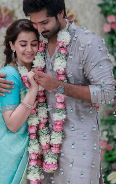 a man and woman standing next to each other in front of a flower lein