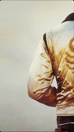 the back of a man's gold jacket with his hands on his hips,