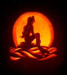 a pumpkin carved to look like a mermaid sitting on the beach in front of a full moon