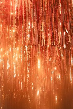 an orange curtain with lots of beads hanging from it's sides and lights in the background