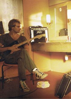 a man sitting on a chair playing a guitar in a room with guitars and other musical equipment