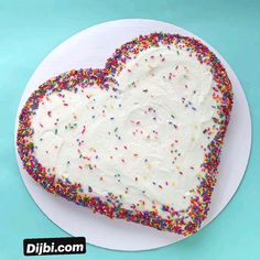 a heart shaped cake on a plate with sprinkles and white frosting