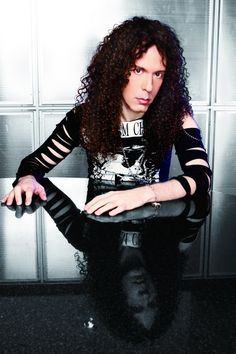 a man with long curly hair sitting in front of a wall holding a black purse