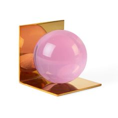 a pink ball sitting on top of a gold plated object in front of a white background