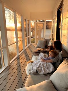 a woman and child are sitting on a porch by the water with their arms around each other