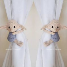 two stuffed animals sitting on top of curtains next to each other, one is wearing a sweater