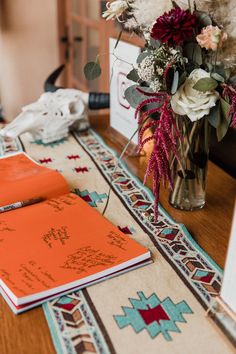 an open book on a table next to a vase with flowers and other items in it