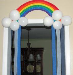 a mirror with balloons hanging from it's sides in front of a rainbow arch