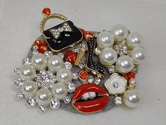 This whimsical brooch is made up of faux white pearls, bright red and clear white rhinestones along with a whimsical black purse, black high heels and red lip charms. The base of this brooch is a smoke grey felt. Each piece is one of a kind and unique.  No two are exactly the same. Wear this brooch as an accent on a dress, sweater, coat, jacket, scarf, shawl, purse or in your hair.  A little sparkle will always make you smile. Wedding Brooches, Wedding Brooch, Dress Sweater, White Rhinestone, Black High Heels, Black Purses, Ornament Wreath, Red Lips, Pearl White