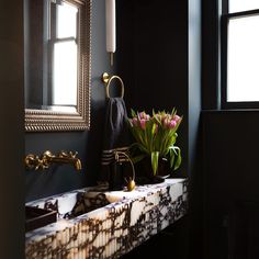 a bathroom sink sitting under a mirror next to a vase with flowers on top of it