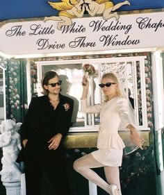 two people standing next to each other in front of a sign that says the little white wedding chapel drive thru windsor