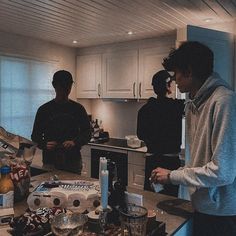 three men standing in a kitchen with food on the counter and one man holding a knife