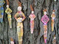 several wooden figures are hanging on a tree trunk in the shape of women and cats