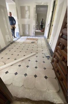 two men are standing in an empty room with tile on the floor, and one man is