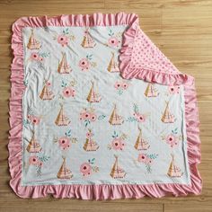 a blanket with pink ruffled edges and sailboats on it, sitting on a wooden floor