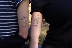 two people with matching tattoos on their arms, one holding the other's arm