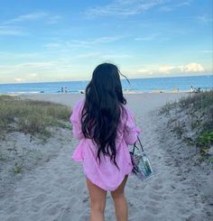 a woman walking down a sandy beach towards the ocean with her back to the camera